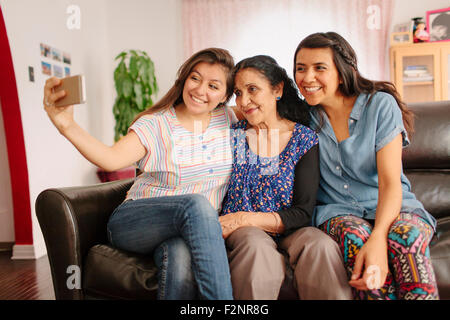 Grandmother and granddaughters taking selfie on sofa Stock Photo