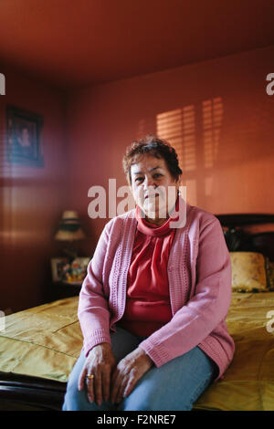 Hispanic woman sitting on bed Stock Photo