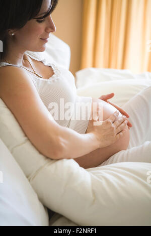 Pregnant woman rubbing her belly on sofa Stock Photo