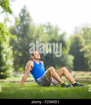 Young athlete sitting on grass in a park and listening to music on headphones with his eyes closed shot with tilt and shift lens Stock Photo