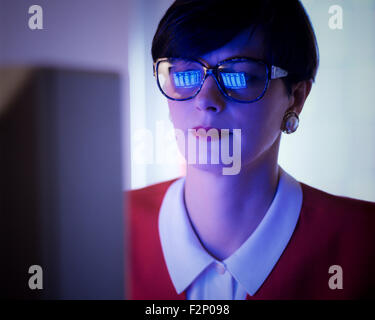 Businesswoman woman with computer screen reflected in her glasses, lit by computer light Stock Photo