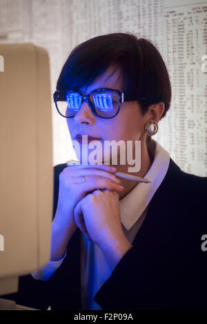 Thoughtful businesswoman with computer screen reflected in her glasses, lit by computer light Stock Photo
