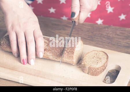 Woman cuts bread loaf on a wooden cutting board Stock Photo