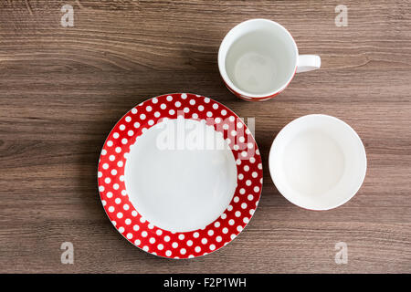 Red polka dotted plate, mug and bowl on brown table Stock Photo
