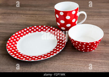Red polka dotted plate, mug and bowl on brown table Stock Photo