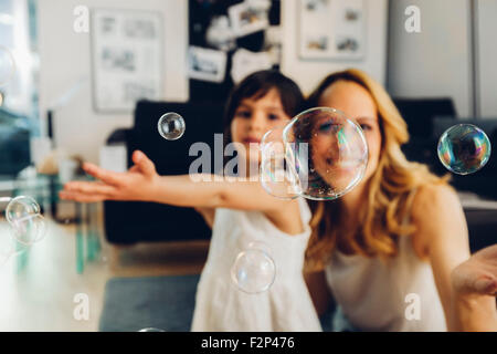 Happy mother with daughter at home blowing soap bubbles Stock Photo