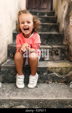 Portrait of laughing little girl sitting on steps Stock Photo