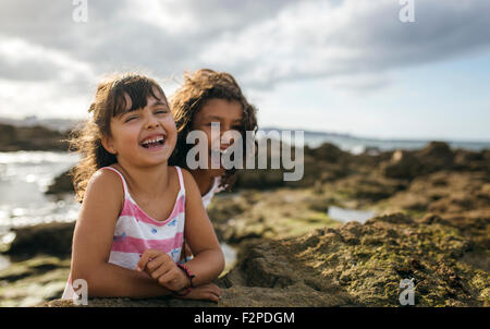 Spain, Gijon, portrait of two laughing little girls at rocky coast Stock Photo