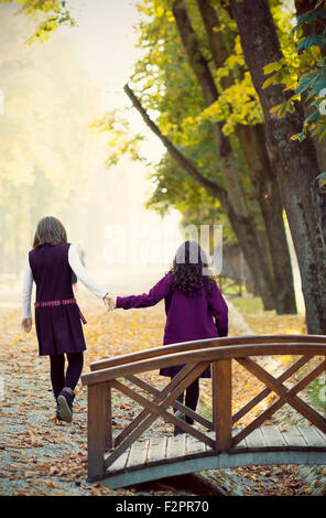 Two school girls holding hands in the autumn park Stock Photo
