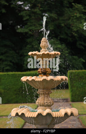 A small sandstone ornate water fountain spouting water which trickles down three tiers to the bottom. Stock Photo