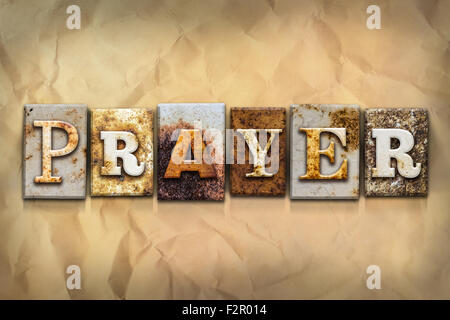 The word 'PRAYER' written in rusty metal letterpress type on a crumbled aged paper background. Stock Photo