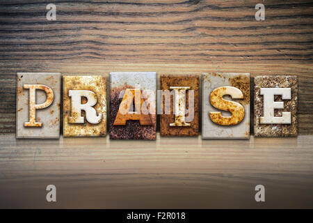 The word 'PRAISE' written in rusty metal letterpress type sitting on a wooden ledge background. Stock Photo