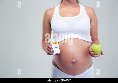 Concept photo of a pregnant woman choosing beetwin cigarettes and apple isolated on a white background Stock Photo