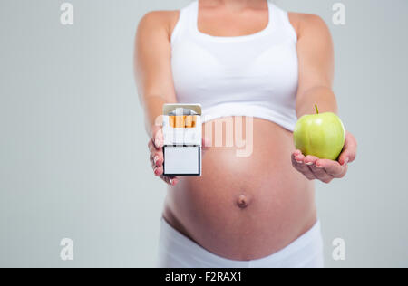 Concept image of a pregnant woman choosing beetwin cigarettes and apple isolated on a white background Stock Photo