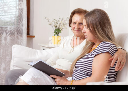 Carer spending time with an elderly woman by reading a book Stock Photo