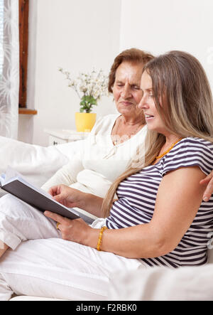 Carer spending time with an elderly woman by reading a book Stock Photo