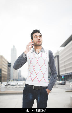 Knee figure of a young handsome indian contemporary business man walking through the city talking smarpthone looking on his left -  technology, network, business, finance concepts Stock Photo