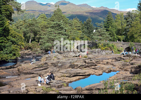 People relaxing on the rocks surrounding the Falls of Dochart at Killin, Scotland with the Tarmachan ridge in the background. Stock Photo