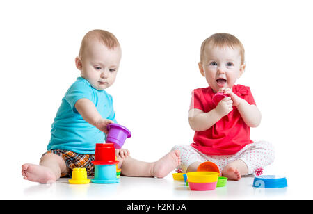 Cute babies playing with color toys. Children girl and boy sitting on floor. Isolated on white background. Stock Photo