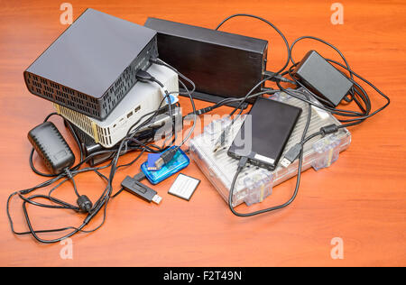 Many memory devices like hard disk drives or memory cards, in format USB or Firewire, with a lot of entangled cables Stock Photo