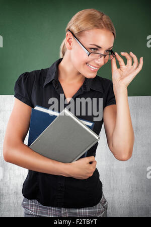 Cute cheerful teacher portrait, smiling woman standing near chalkboard, working in the university, back to school Stock Photo