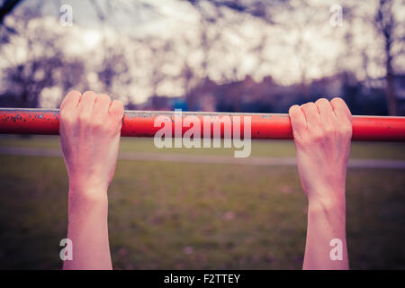 Closeup on a young woman's hands as she is hanging from a monkey bar in the park Stock Photo