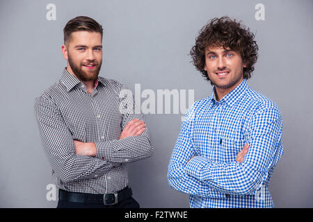 Portrait of a two happy men standing with arms folded on gray background Stock Photo