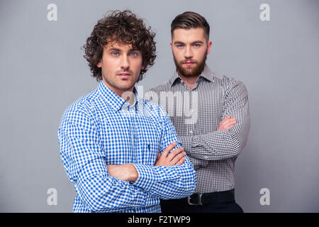 Portrait of a two serious casual businessmen standing with arms folded on gray background Stock Photo