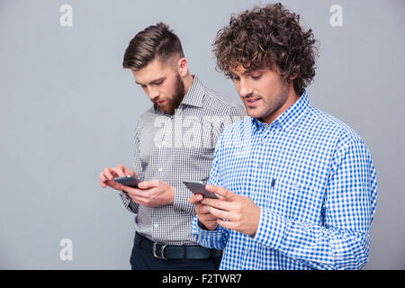 Portrait of a two serious men using smartphone over gray background Stock Photo