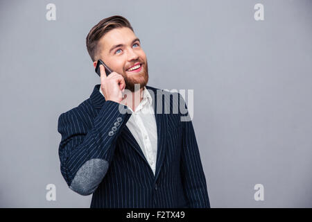 Portrait of a happy thoughtful businessman talking on the phone and looking up over gray background Stock Photo