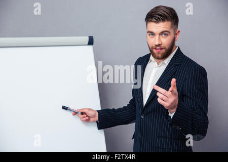 Portrait of a young businessman in suit presenting something on blank board over gray background Stock Photo