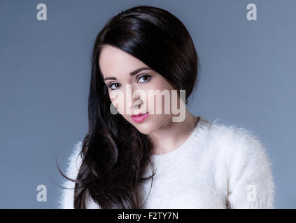 beautiful dark haired woman in white sweater on blue background Stock Photo