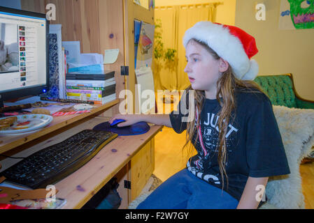 Long haired boy with santa hat using computer. Stock Photo