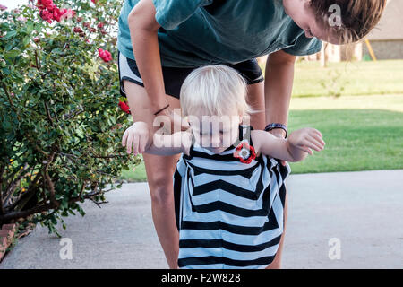 A one year old Caucasian baby girl walks with the help of her aunt. USA Stock Photo