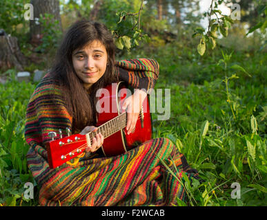 Young girl plays guitar sitting on the grass in the Park. Stock Photo