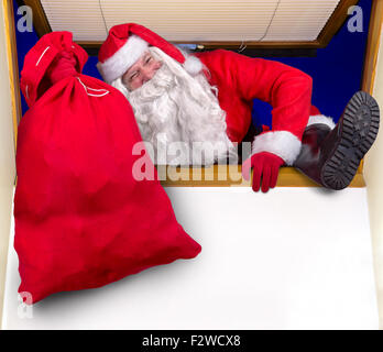 Santa Claus carrying a bag of gifts and climbs into the room through the window Stock Photo