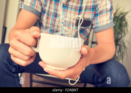 closeup of young caucasian man having a cup of coffee or tea and listening to music form his smartphone Stock Photo