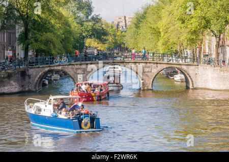 Boats pass underneath a bridge on the Amstel river, Amsterdam Stock Photo