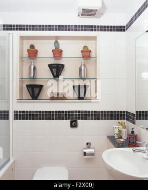 Black mosaic tiled border in modern white bathroom with glass shelves in alcove above toilet Stock Photo