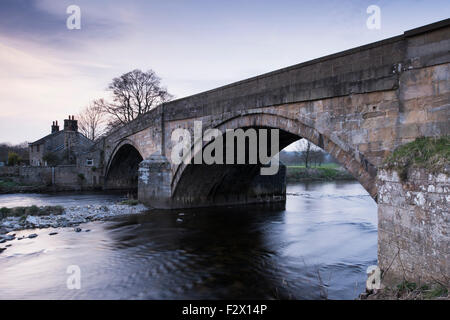 Scenic view at sunset, of traditional, old, stone, road bridge over flowing water of River Wharfe near Bolton Abbey, Yorkshire Dales, England, UK.