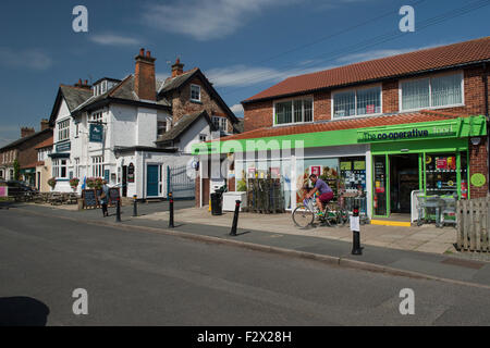 Village scene - man cycling away from Co-operative Food convenience store & lady walking along the road by pub - Upper Poppleton, York, England, UK. Stock Photo