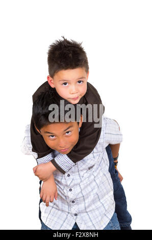 Two small hispanic boys playing, one carrying the other on his back, facing camera Stock Photo