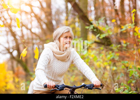 Active senior woman riding bike in autumn nature. They having romantic time outdoor. Stock Photo