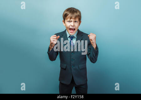 a  boy of twelve European appearance  in a suit shouting angry on a gray  background Stock Photo