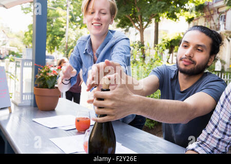 Young man and woman outdoors at a cafe, one trying to recork a bottle of wine. Stock Photo