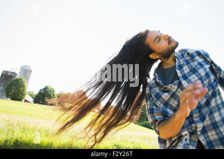 A young man letting down his very long dark hair and shaking his head to fan it out in the fresh air. Stock Photo