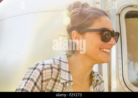 A young woman wearing sunglasses by a silver coloured trailer. Stock Photo