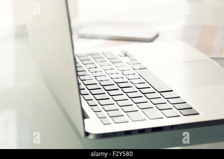 Laptop on modern glass table in office. Focus on keyboard Stock Photo