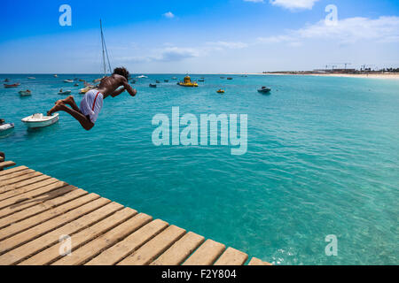 Teenage Cape verdean boy jumping on the turquoise  water of Santa Maria beach in Sal Cape Verde - Cabo Verde Stock Photo