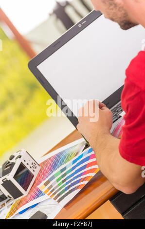 Man working on laptop with palette, colormap spread out next to it Stock Photo